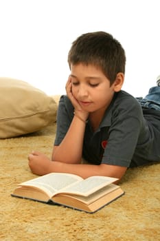 Boy in a room reading a book over a carpet. 