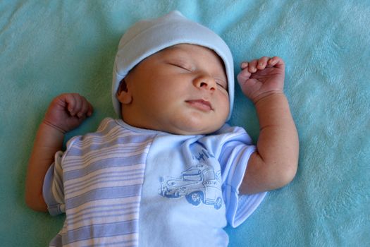 Week old baby boy on a blue blanket early in the morning, fast asleep