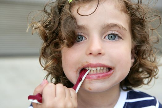 Little blue eyes girl eating sweet candy with dirty face