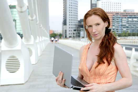 Beautiful redhead woman in downtown bridge with laptop