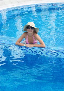 Smiling woman in swimming pool with hat and sunglasses
