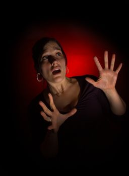Scared woman with open hands in protective position, with red spot on black background