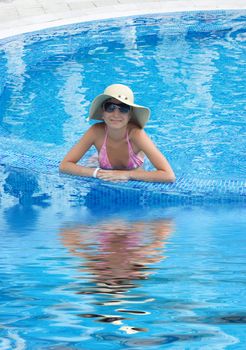 Smiling woman in swimming pool with hat and sunglasses with reflection