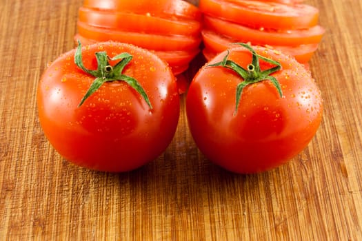 Picture of two tomatoes on a wooden board with sliced tomatoes in the back