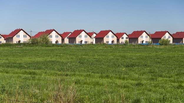New cottages with red roofs and field of green grass