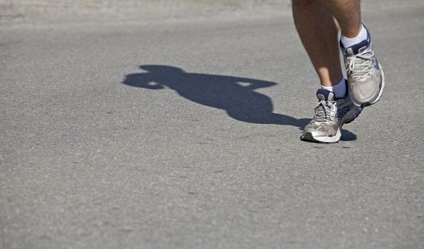 feet and shadow of a jogger on asphalt