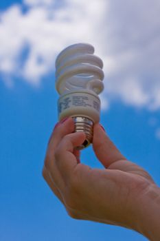female teen holding a compact fluorescent light bulb up with a cloudy blue sky