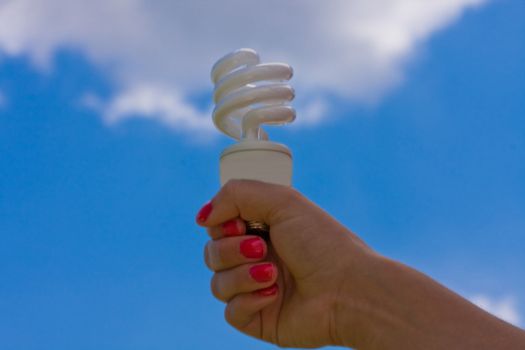female teen holding a compact fluorescent light bulb up with a cloudy blue sky