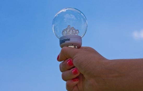 female teen holding a light bulb up with a cloudy blue sky