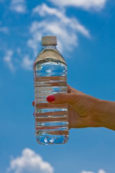 teen girl holding a water bottle up with a blue cloudy sky