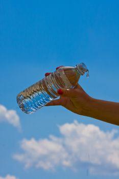 teen girl holding a water bottle up with a blue cloudy sky