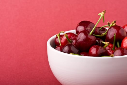 white bowlful of red cherries solid background