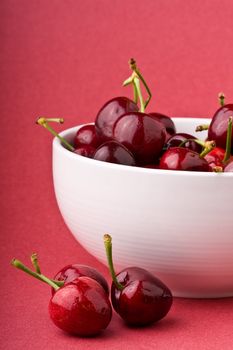 white bowlful of red cherries solid background