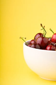 white bowlful of red cherries solid background