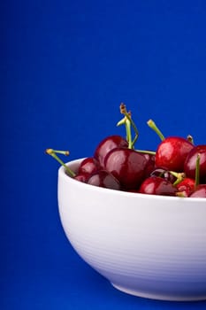 white bowlful of red cherries solid background