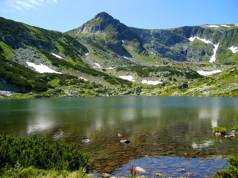 green rock mountain reflected in clear lake