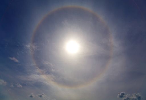 Circles halo in the blue cloudy sky around of the sun