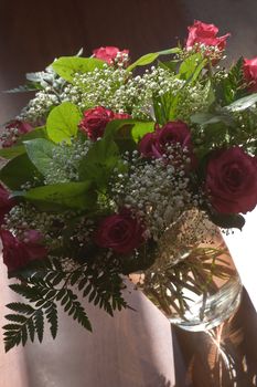 Glass vase in sunlight with red roses and gypsy or baby's breath