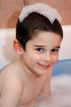 Smiling cute little boy in a bathtub with foam cap on his head