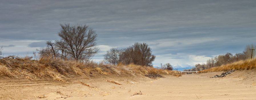 A wide view shot of a dry canal.  It has been a long winter.  The canal is begging the mountains, in the background, for more water.