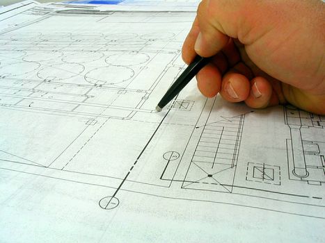 This is a drafters hand with pen carefully looking over a black line drawing. 