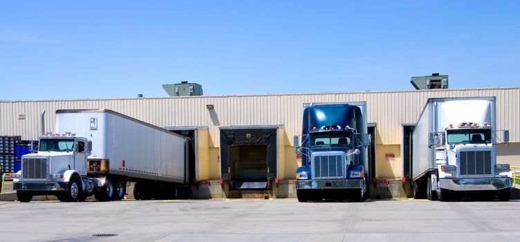 This is a picture of 18 wheeler semi trucks loading at a warehouse building.