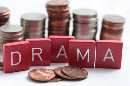 Wooden letters spelling the word "Drama" in front of stacks of dollar coins