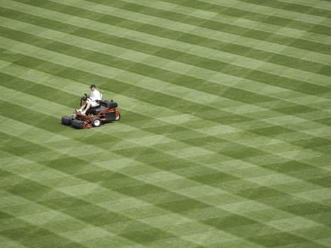 A solitary man (unidentifiable) mows a huge field into stripes