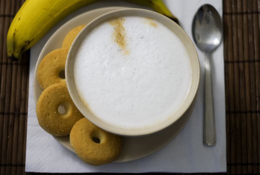 Breakfast with a cup of cappuccino with four biscuits and a banana