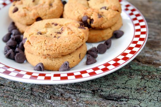 Chocolate chip cookies on a plate with chocolate chips laying around the cookies.