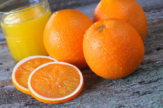 Fresh oranges whole and sliced with a fresh glass of OJ in the background.