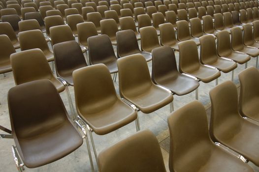 Endless rows of empty brown plastic seats in an exhibition hall.