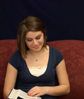 A pretty teenage girl sitting on a sofa studying a textbook.