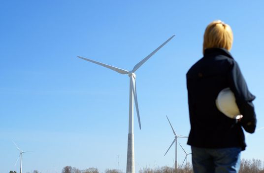 Woman engineer or architect with white safety hat and wind turbines on background        