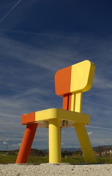A huge chair towers over distant houses, against a rich blue sky.