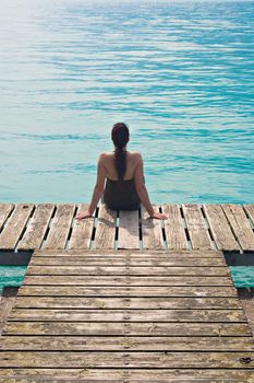 Woman sitting on wooden pier, contemplating a turquoise lake.