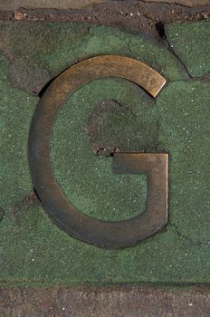 The letter G is encased in green marble on the sidewalk in downtown Denver.