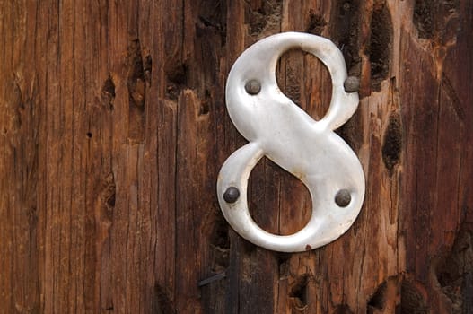 A metal number 8 is attached to a rough, worn telephone pole.