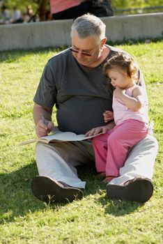 The grandfather with grand daughter sitting on a grass in park