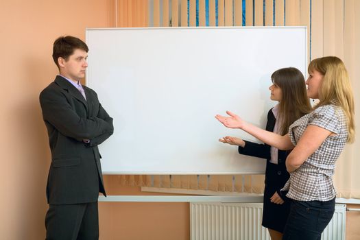 Office workers discuss work standing at a board