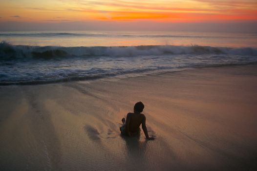 Boy on the beach with waves rolling towards him. Dreamland beach, Bali, Indonesia.