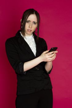 Young business woman reading message on her smart phone with disturb expression against pink background