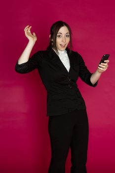 Young business woman reading message on her smart phone with a surprise expression against pink background