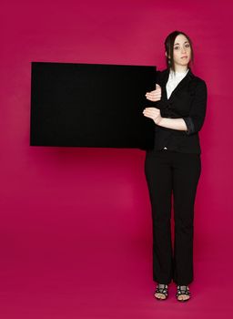 Young business woman wearing a business suit holding a black board against pink background