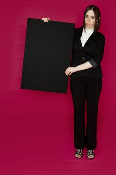 Young business woman wearing a business suit holding a black board against pink background