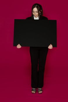 Young business woman wearing a business suit standing behind looking down at a black board against pink background