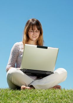 Happy young girl smiling and working on a laptop outdoors