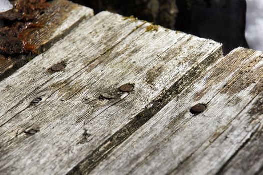 Old weathered wood plank of a deck with focus on rusted nail on a winter day.