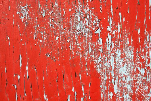 Intense red background with old bright paint on exterior door peeling showing the grey underneath.