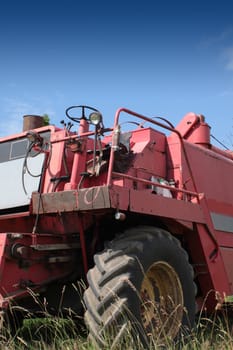 The front end of a red combine harvester machine stationary in a farm field in rural Wiltshire, England, set against a blue summer sky.